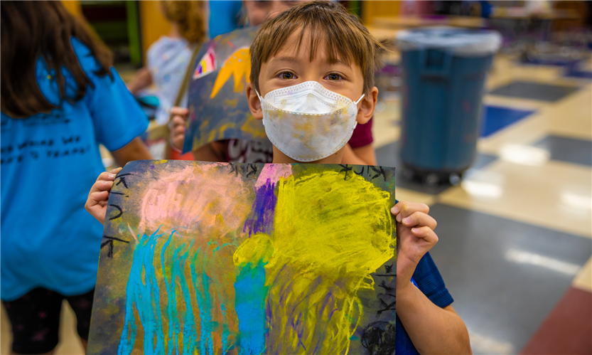 A boy wearing a mask holds up a piece of art